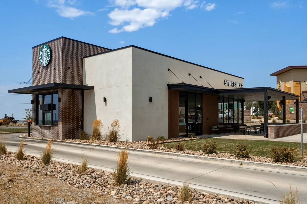 Starbucks retail building viewed from the front corner, with brick and light stucco walls, glazing and covered seating.